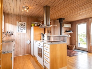 Ett kök med träpanel på väggarna, en köksö i mitten, en spis och ett diskho.
