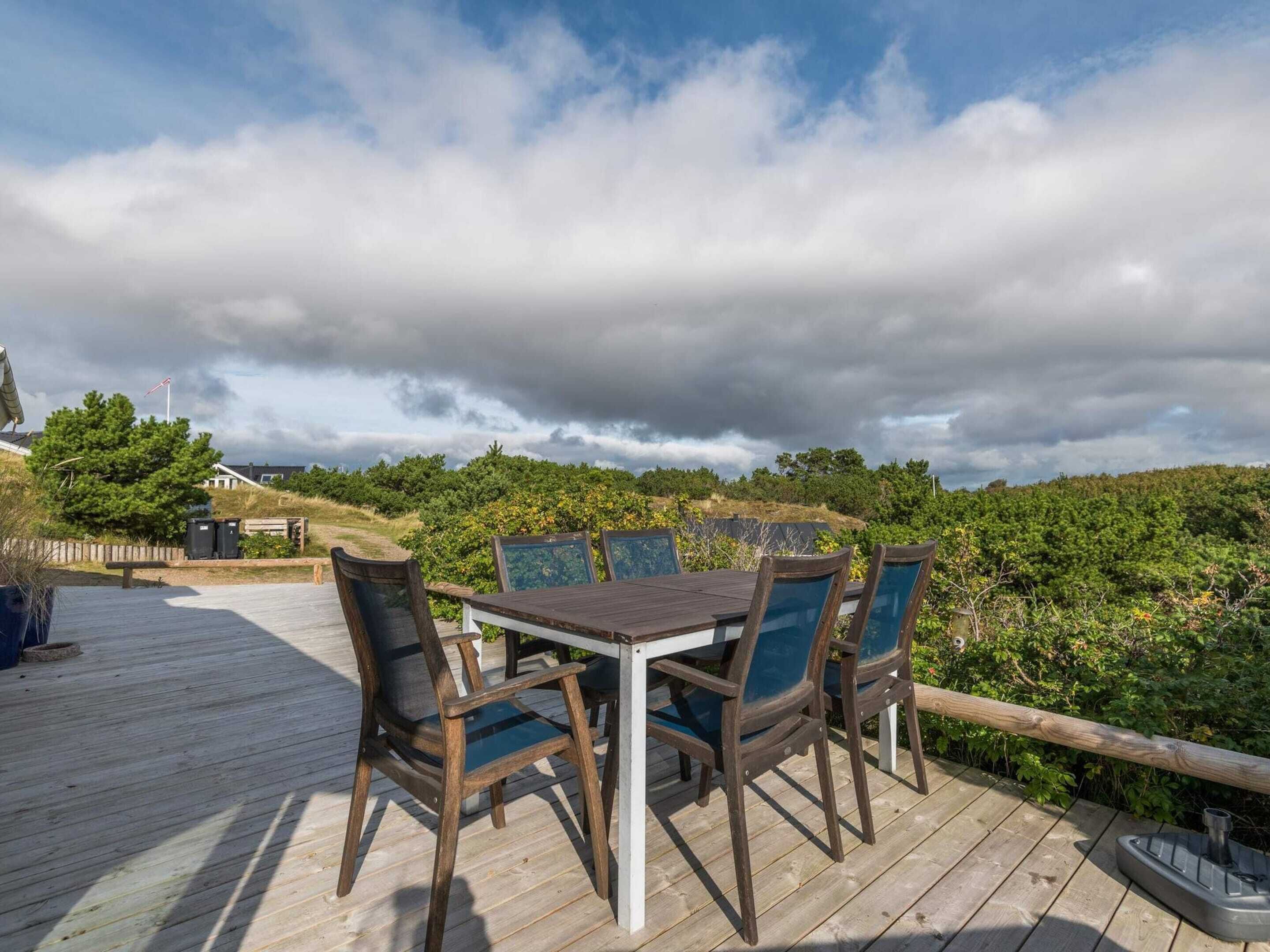 A wooden deck with a table and chairs, overlooking a forested area.