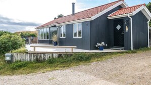 Ein modernes, zweistöckiges Haus mit rotem Ziegeldach, großen Fenstern und einer Holzterrasse.