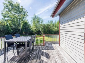 A wooden deck with a table and chairs, surrounded by a white fence and greenery.