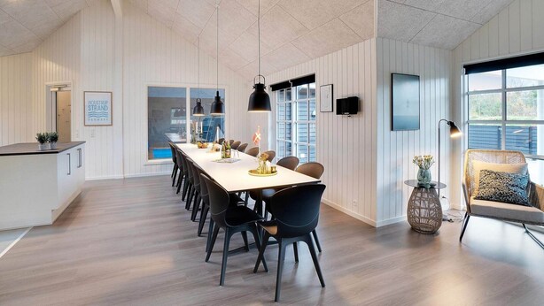 Een moderne eetruimte met een lange tafel, zwarte stoelen, hanglampen en uitzicht op de omgeving.