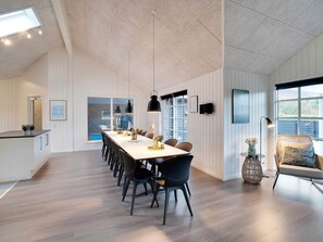 A modern dining area with a long table, black chairs, pendant lights, and a view of the outdoors.