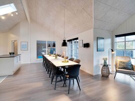 Un comedor moderno con una mesa larga, sillas negras, lámparas colgantes y vistas al exterior.