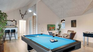 Een pooltafel in een ruimte met een hoge nok, een bar en een zithoek met een tafelvoetbal.