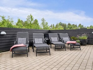 A patio area with four lounge chairs, a black wall, and a brick floor.
