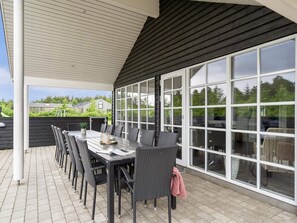 An outdoor patio with a table and chairs, large windows, and a view of the surrounding area.