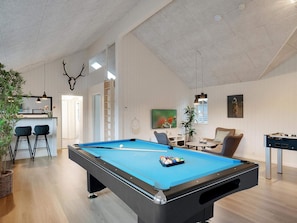 A pool table in a room with a high ceiling, a bar area, and a seating area with a foosball table.