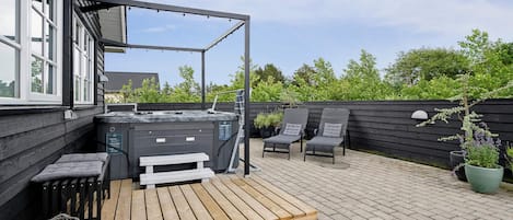 A rooftop patio with a hot tub, two lounge chairs, and a wooden deck.