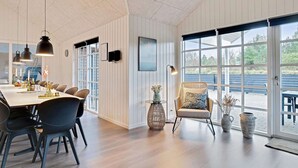 Een moderne eetruimte met een lange tafel, stoelen, hanglampen en uitzicht door grote ramen.