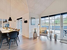 Un comedor moderno con una mesa larga, sillas, lámparas colgantes y vistas amplias por las ventanas.