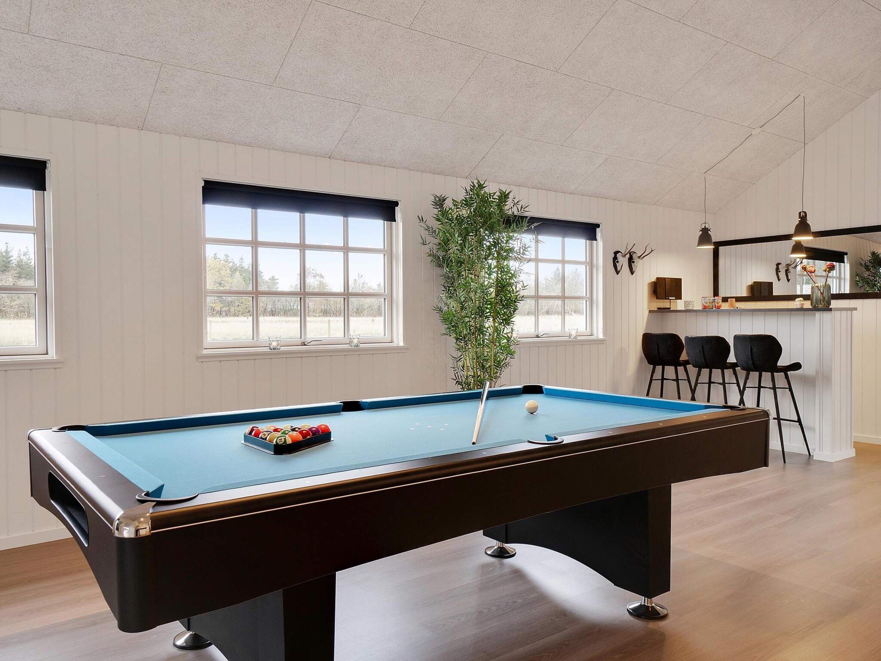 A pool table with balls, a potted plant, and a bar area with stools.