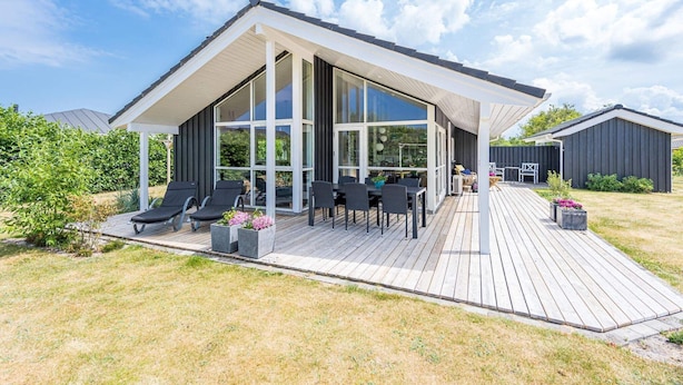 Et moderne hus med stor terrasse, udendørs møbler og en overdækket patio.