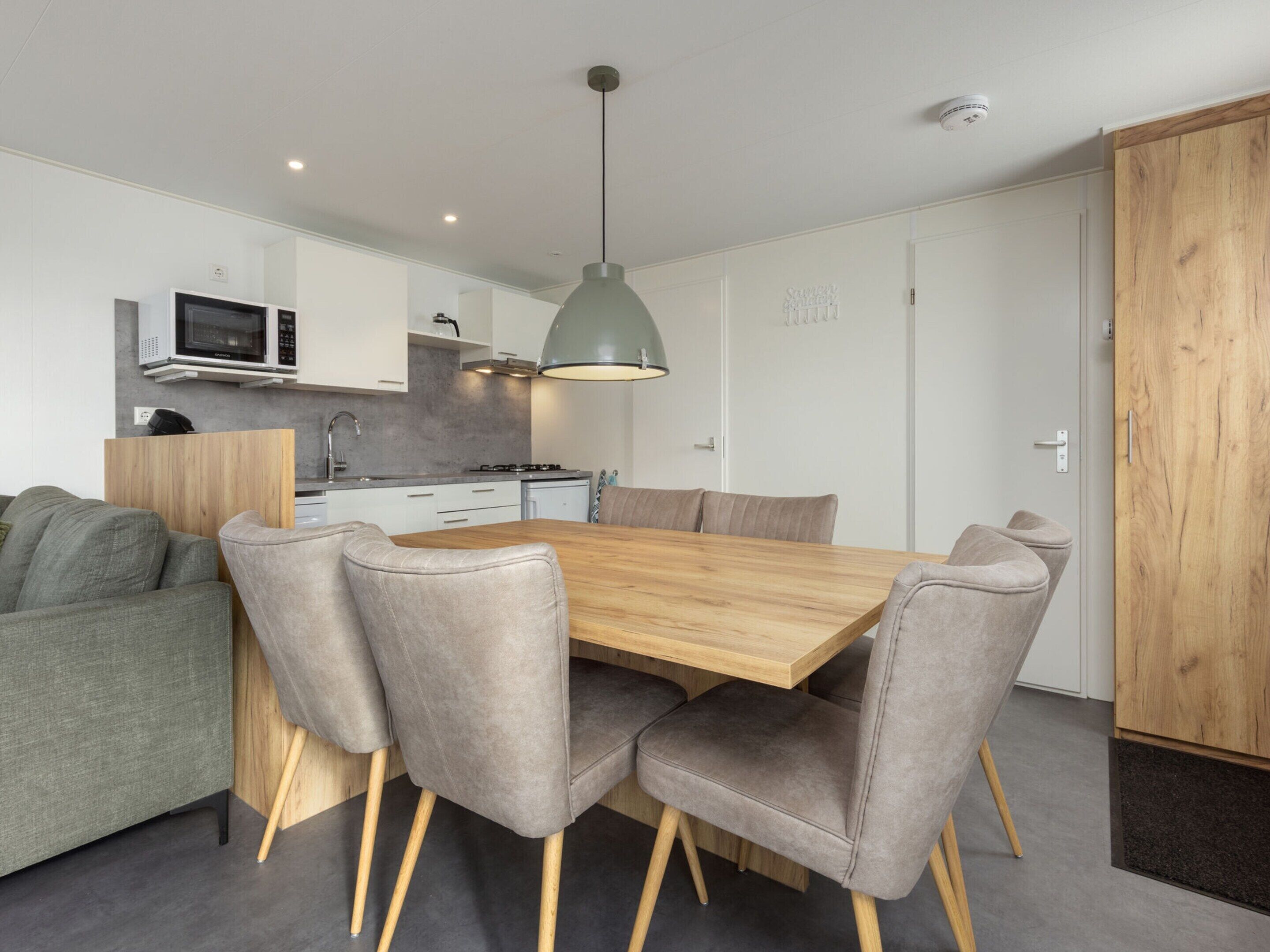 A modern kitchen with white cabinets, a microwave, and a stove. There is a dining table with four chairs and a pendant light above it.