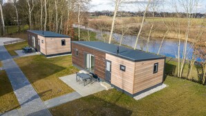 Two modern cabins with a view of a lake, wooden exterior, and a patio with outdoor furniture. - Modern Chalet Near Forest (Gasselternijveen)