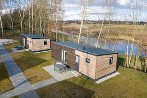 Two modern cabins with a view of a lake, wooden exterior, and a patio with outdoor furniture. - Modern Chalet Near Forest (Gasselternijveen)