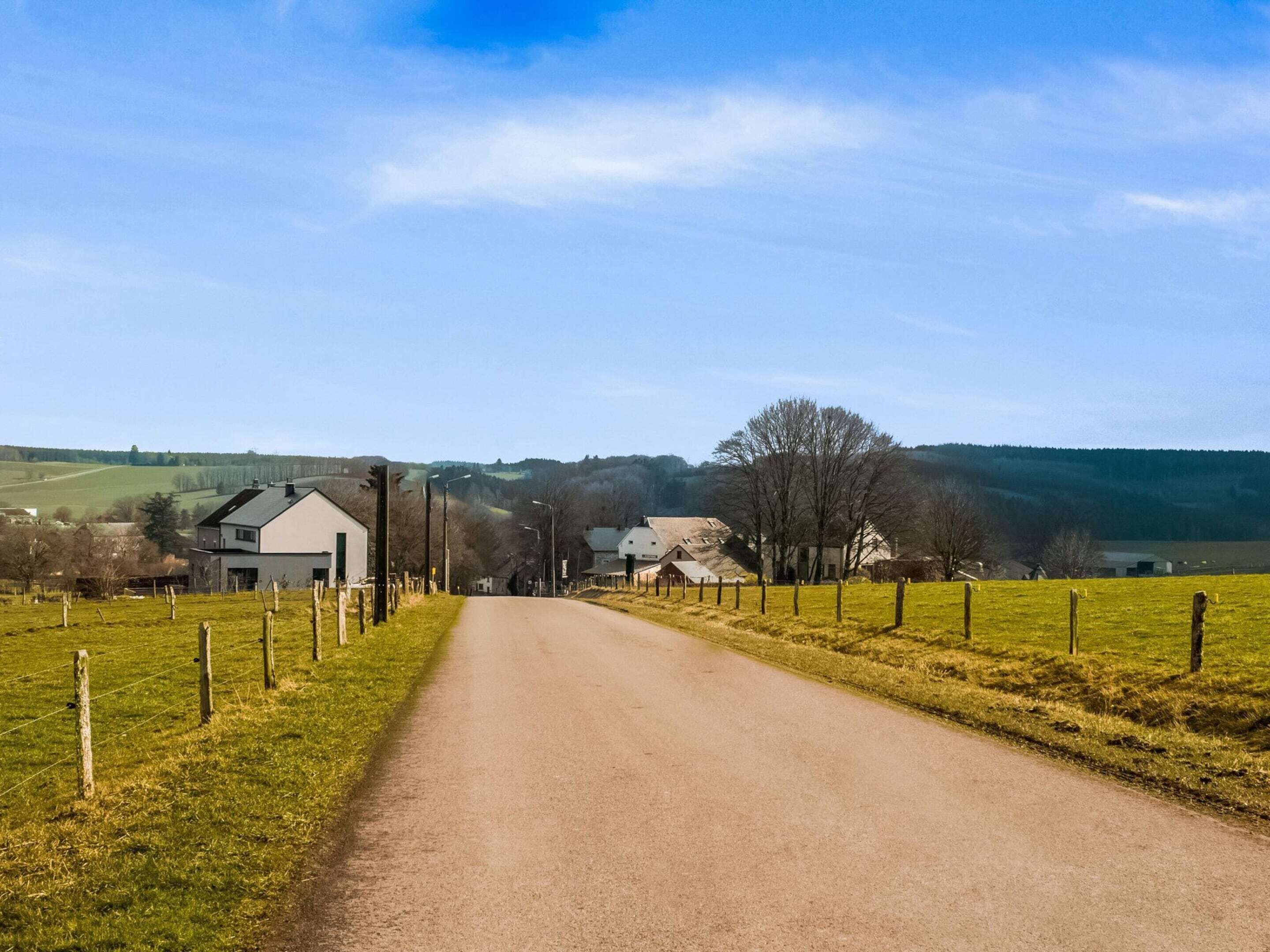 A rural road flanked by houses and fields under a clear sky.