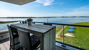 A balcony with a view of a calm lake, a wooden table, and chairs. - Apartment in Veere With Lake Views & Marina (Kamperland)