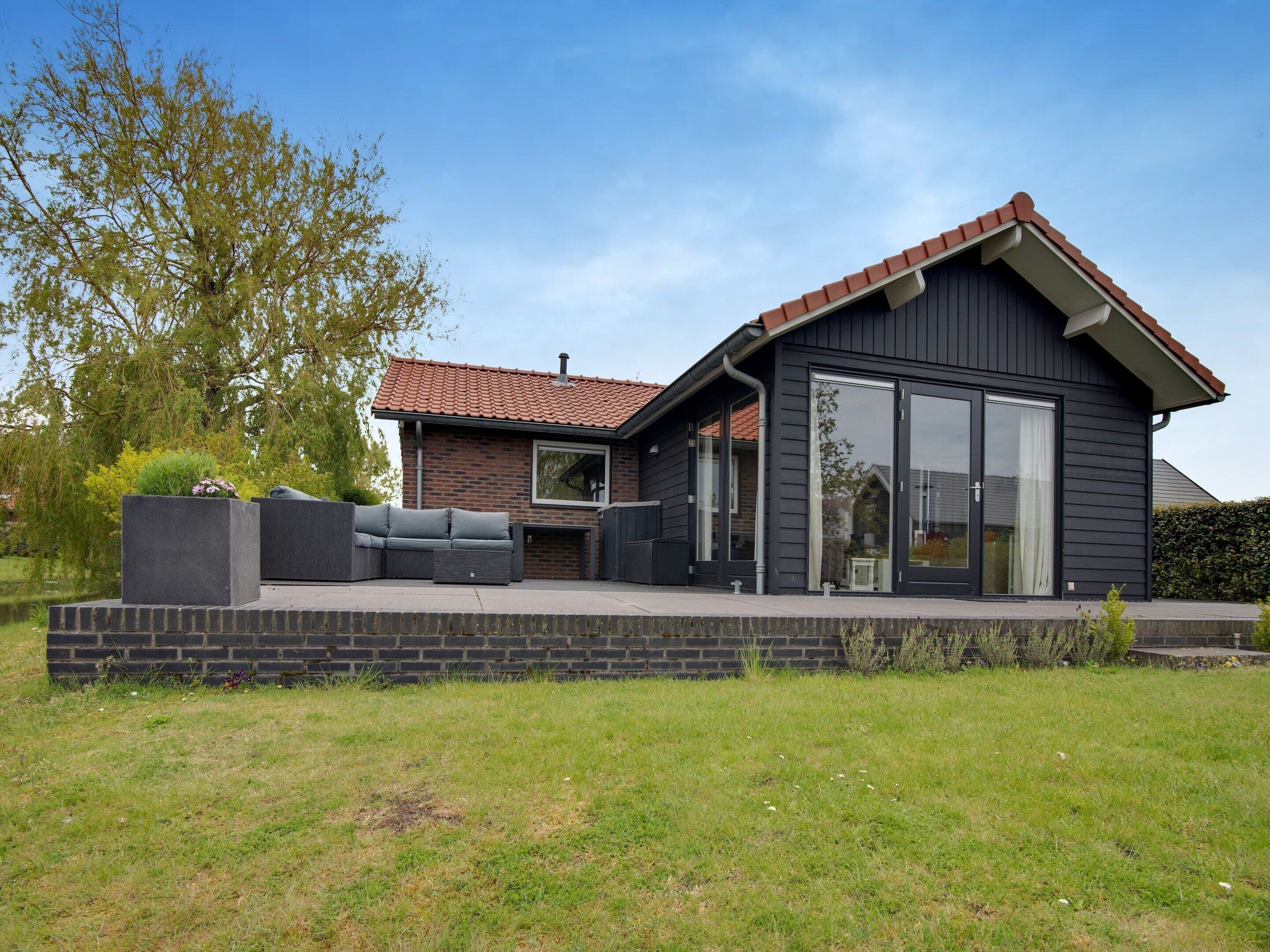 Ein modernes Haus mit Terrasse, einer großen Schiebetür und einem Kamin aus Ziegelsteinen.