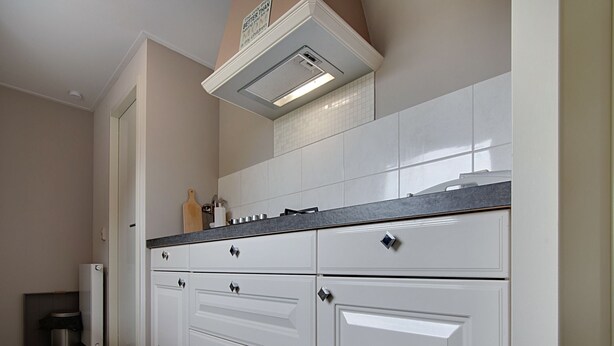 A kitchen with white cabinets, a black countertop, and a vent above the sink. - Holiday Home in Kattendijke Near National Park (Kattendijke)