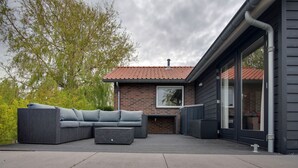 A modern outdoor patio with a sectional sofa, a fire hydrant, and a brick building with a tiled roof. - Holiday Home in Kattendijke Near National Park (Kattendijke)