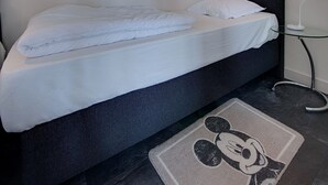 A bed with white bedding, a dark headboard, a Mickey Mouse rug, and a bedside table with a lamp. - Holiday Home in Kattendijke Near National Park (Kattendijke)