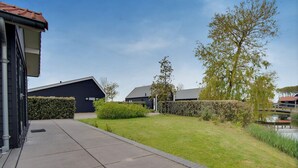 A residential area with a paved walkway, a small pond, and two houses with dark roofs. - Holiday Home in Kattendijke Near National Park (Kattendijke)