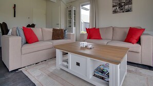 A living room with two beige sofas, a wooden coffee table, and a white cabinet with magazines. - Holiday Home in Kattendijke Near National Park (Kattendijke)