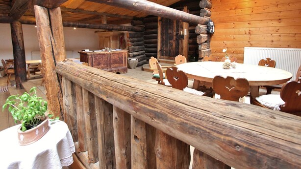 A rustic wooden interior with a round dining table, heart-shaped chairs, and a wooden bench.