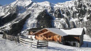 A wooden cabin with a balcony, surrounded by snow-covered mountains.