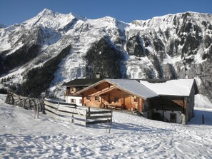 A wooden cabin with a balcony, surrounded by snow-covered mountains.