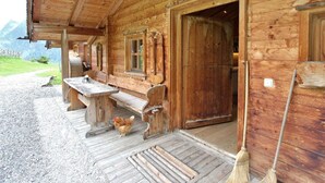Uma cabana de madeira com varanda, uma mesa, bancos e uma galinha.