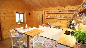 Interior acolhedor de uma cabana de madeira, com cozinha que inclui armários brancos, mesa de jantar de madeira e janela com vista para o exterior.