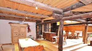 A rustic wooden interior with a dining area, wooden chairs, a bar, and a fireplace.