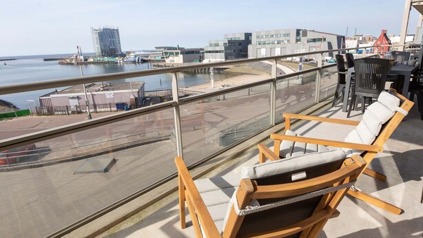 A balcony with wooden chairs and a view of the waterfront, including buildings and a marina. - Sea-view Apartment in Den Haag near Beach (The Hague)