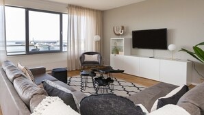 A modern living room with a sofa, a dining table, and a TV. - Sea-view Apartment in Den Haag near Beach (The Hague)