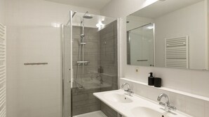 A modern bathroom with a glass-enclosed shower, a white sink with two faucets, and a large mirror above the sink. - Sea-view Apartment in Den Haag near Beach (The Hague)
