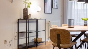 A modern dining area with a round table, chairs, pendant lights, a plant, and a shelf with decorative items. - Sea-view Apartment in Den Haag near Beach (The Hague)
