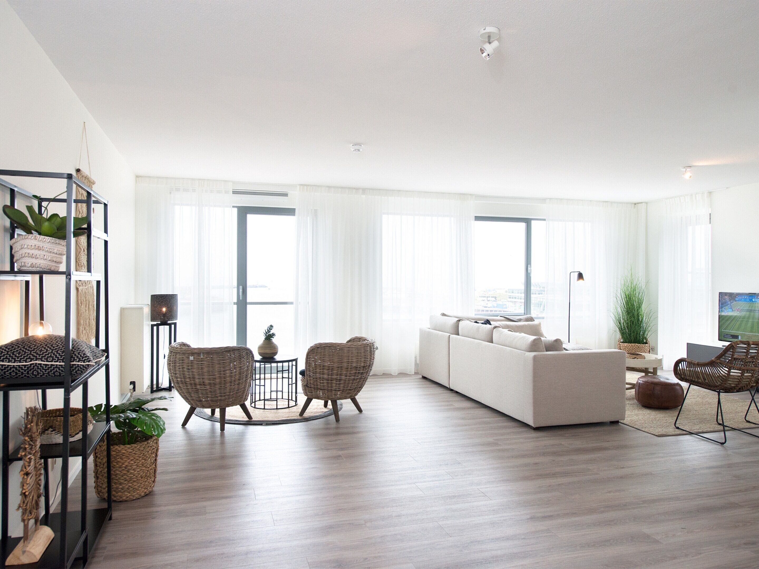 A spacious living room with a sofa, two wicker chairs, a coffee table, and a TV.