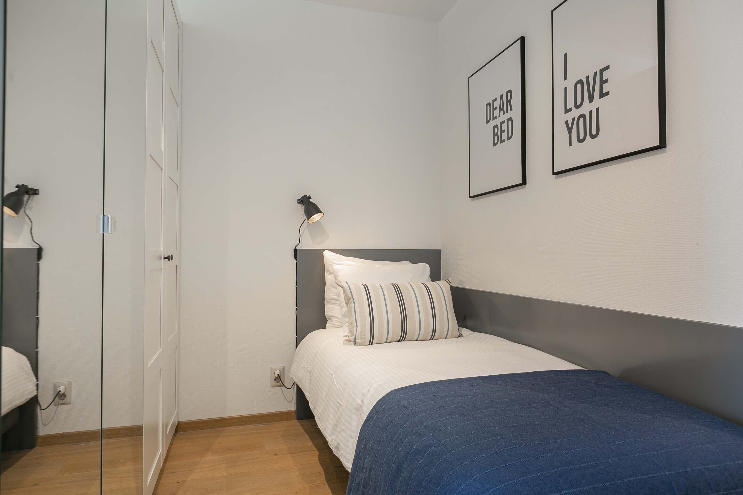 A bedroom with a bed, a wardrobe, and two wall-mounted lamps.
