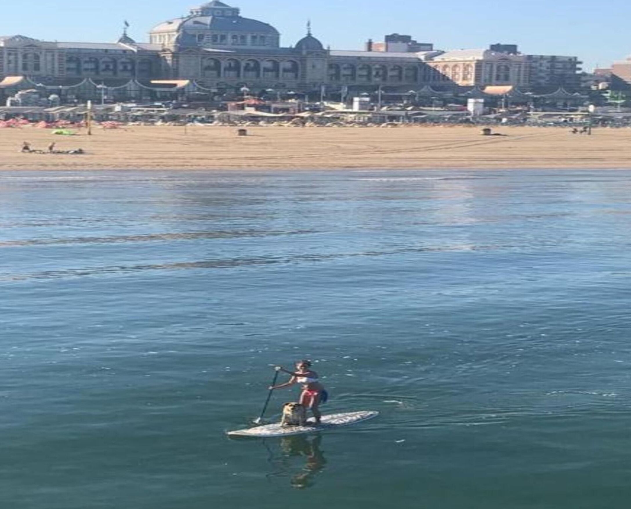 A person paddleboarding on a calm body of water with a large building in the background.