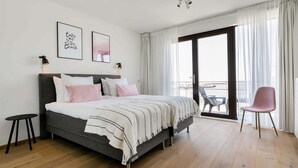A bedroom with a bed, a small table, a chair, and a balcony with a view. - Apartment in Den Haag With sea Beach (The Hague)