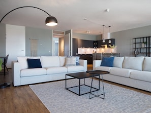 A modern living room with a sofa, coffee table, and a kitchen in the background. - Apartment in Den Haag for 5 Person (The Hague)