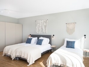 A modern bedroom with two beds, a large wardrobe, and macramé wall hangings. - Apartment in Den Haag for 5 Person (The Hague)