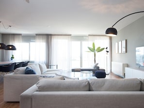A modern living room with a sofa, a dining table, and a plant. - Apartment in Den Haag for 5 Person (The Hague)