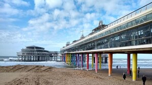 Une jetée aux piliers colorés et une structure de verre qui s’étend au-dessus de la plage.