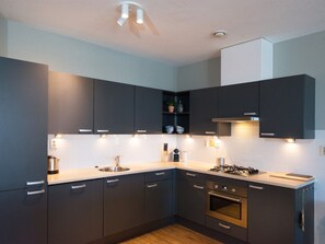 A modern kitchen with dark cabinetry, a stainless steel sink, and a built-in oven. - Apartment in Den Haag for 5 Person (The Hague)