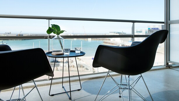 Un balcon avec deux chaises noires, une petite table et un pot de fleurs.