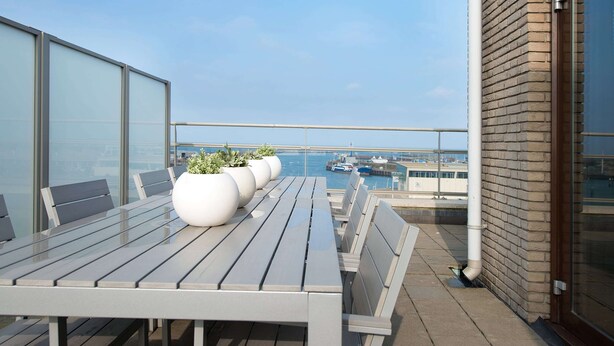 Un balcón con una mesa y sillas, plantas en macetas y vistas al puerto deportivo.