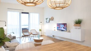 A modern living room with a wooden dining table, wicker chairs, a large TV, and a balcony with a view. - Ground Floor Apartment near Scheveningen (The Hague)