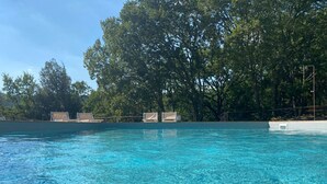 Une piscine d’un bleu éclatant, avec des chaises longues et des arbres en arrière-plan.